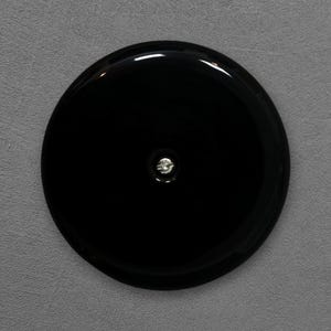 Może przedstawiać: Błyszczący czarny, okrągły przedmiot z małym, srebrnym detalem pośrodku. Obiekt ma odblaskową powierzchnię, na szarym tle.