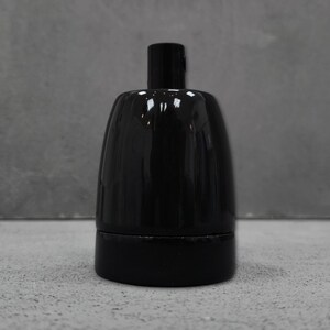 May include: A glossy black ceramic light socket featuring a cylindrical base and a smooth, rounded top section. The electrical component has a uniform dark finish with a reflective surface, designed for standard light bulb installation and wiring.