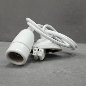 Op de afbeelding: Een witte keramische lampfitting met een cilindrische fitting en een ronde basis. Een wit gevlochten snoer is bevestigd. De fitting heeft een eenvoudig, modern ontwerp. De elektrische connectoren zijn zichtbaar.