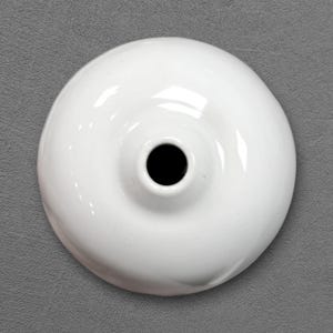 Pode incluir: Um objeto circular de cerâmica branca com um acabamento liso e brilhante e uma abertura central oca. A peça apresenta um perfil arredondado em forma de cúpula que se estreita em direção ao meio, criando uma estrutura simétrica em taça.