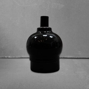 May include: A glossy black ceramic light socket featuring a rounded, bulbous body with a smooth, reflective finish. The fixture has a cylindrical top section and a wider, cylindrical base, designed for electrical lighting applications.