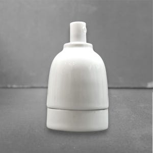 Op de afbeelding: Een witte keramische lamphouder met een cilindrische bovenkant en een afgeronde behuizing. De lamphouder heeft een gladde, glanzende afwerking. Ontworpen om een gloeilamp te bevatten. Het ontwerp is eenvoudig en functioneel.