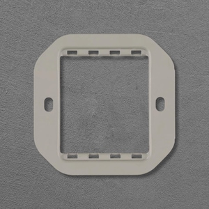 Op de afbeelding: Een witte, vierkante afdekking voor een stopcontact met afgeronde hoeken. De afdekking heeft een rechthoekige opening in het midden en twee ovale schroefgaten. Kleine rechthoekige sleuven zijn gelijkmatig verdeeld langs de bovenrand.