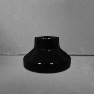May include: A glossy black ceramic base with a wide, circular bottom that tapers upward into a smaller, cylindrical top opening. The object features a smooth, reflective surface and a solid, heavy-looking construction with a uniform dark finish.