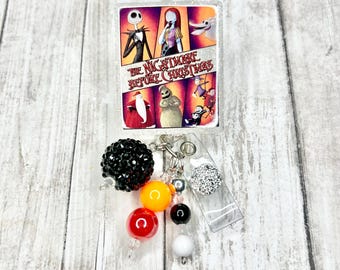 May include: A badge reel featuring a rectangular image from "The Nightmare Before Christmas" with Jack Skellington, Sally, and other characters. The reel has a black beaded ball, colourful beads, and a clear plastic clip.