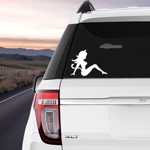 May include: White silhouette decal of a woman with a tail, sitting on a car window. The decal is on a white SUV with a black window.