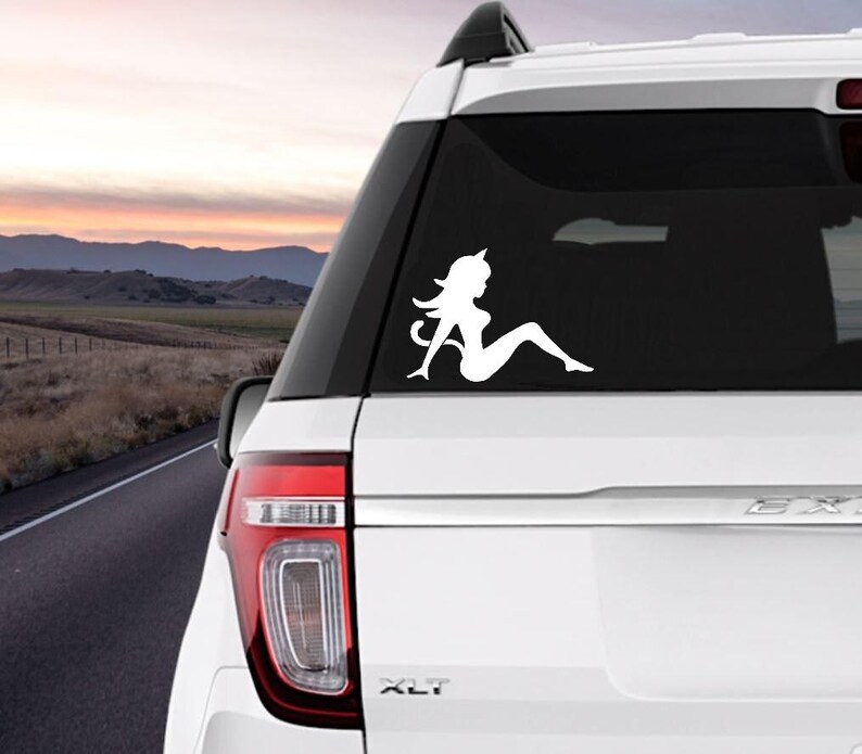 May include: White silhouette decal of a woman with a tail, sitting on a car window. The decal is on a white SUV with a black window.