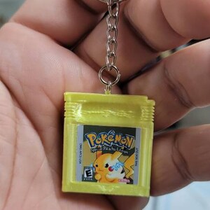 May include: A yellow Game Boy Color keychain with a Pokemon Special Pikachu Edition game cartridge. The keychain has a silver chain and a silver ring.
