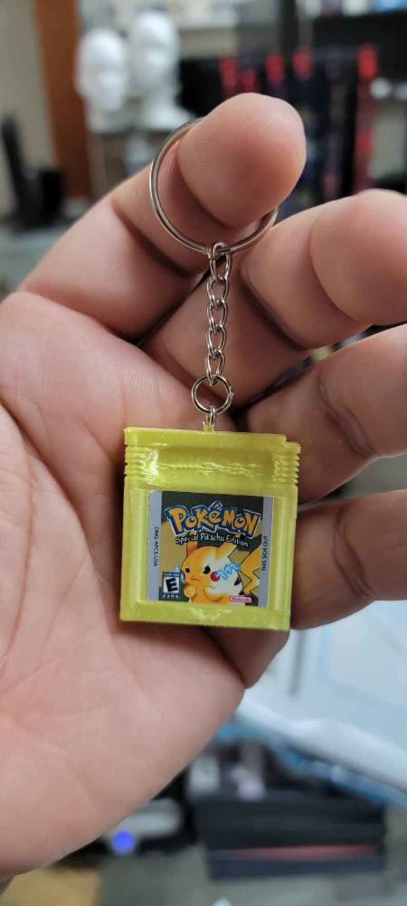 May include: A yellow Game Boy Color keychain with a Pokemon Special Pikachu Edition game cartridge. The keychain has a silver chain and a silver ring.