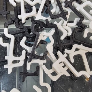 May include: A pile of black and white plastic door stops. The door stops are shaped like a right angle with a curved top.