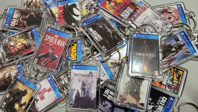 Puede incluir: Una colecci&oacute;n de llaveros de videojuegos con varios t&iacute;tulos populares, incluyendo "Call of Duty: Black Ops", "Spider-Man", "The Last of Us", "Dark Souls" y "NieR: Automata". Los llaveros est&aacute;n hechos de pl&aacute;stico transparente y presentan la portada del juego.