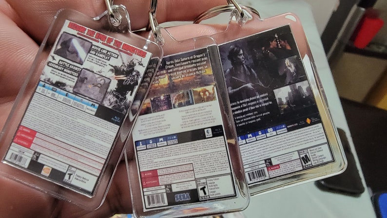 Puede incluir: Tres llaveros de videojuegos con estuches de pl&aacute;stico. Los llaveros presentan las portadas traseras de los juegos "Monster Hunter World", "Yakuza 6: The Song of Life" y "Detroit: Become Human".