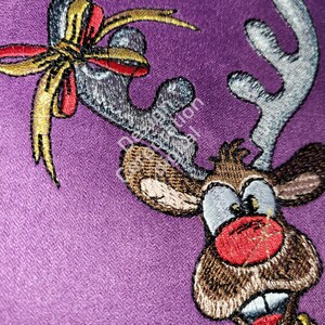 May include: Embroidered reindeer with a red nose and a gold bow on a purple background.