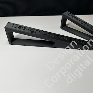 Könnte beinhalten: Zwei schwarze Telefonständer aus Kunststoff mit dem Text "Design Corporation" auf der Vorderseite.