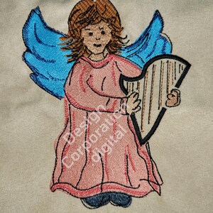 Puede incluir: Imagen bordada de un ángel con alas azules tocando un arpa. El ángel lleva un vestido rosa y tiene el pelo castaño.