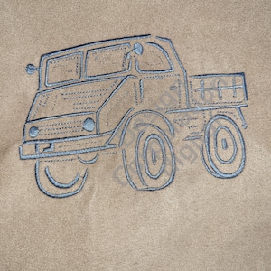 May include: Embroidered design of a vintage truck in light blue thread on a tan fabric. The truck features detailed stitching, including the cab, wheels, and cargo bed. The design is centered on the fabric.
