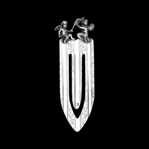 May include: Silver bookmark with two cherubs holding a banner at the top. The bookmark has an ornate design with a decorative loop.