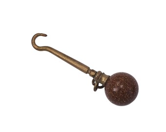 May include: A brass hook with a brown, speckled ball on the end. The hook is curved and the ball is smooth.
