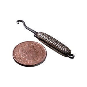 May include: A small, silver-coloured, pocket-sized hook tool with a textured handle. The tool is about the size of a British one-pence coin.