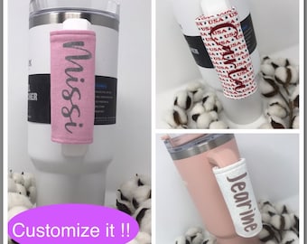 Puede incluir: Tres vasos de acero inoxidable con fundas de tela personalizadas. Las fundas son de color rosa con texto plateado, blanco con texto rojo, blanco y azul, y blanco con texto negro. El texto en las fundas dice "Missi", "USA" y "Jearine".
