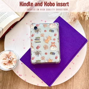Puede incluir: Inserto transparente para Kindle y Kobo con fondo azul claro y un patrón de gatos, libros, plantas y tazas de café. El inserto está sobre un libro morado, un plato blanco y rosa decorado y una superficie de madera. El texto en el inserto dice "PRINTED ON HIGH QUALITY CARDSTOCK".