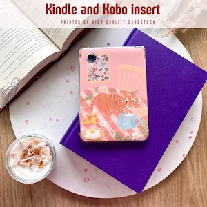 Könnte beinhalten: Eine rosa Kindle- und Kobo-Hülle mit einer Katzenillustration, die auf einem lila Buch liegt. Die Hülle zeigt eine Katze mit einer Tasse, Blumen und einem Cupcake-Design. Der Text "Kindle and Kobo insert" ist sichtbar.