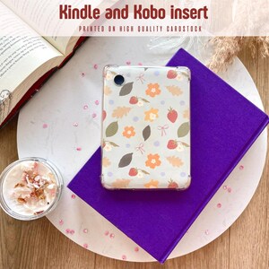 Puede incluir: Un inserto transparente para Kindle y Kobo con un estampado floral de fresas, hojas y flores. El inserto está sobre un libro morado, con un libro abierto y un vaso pequeño de crema con pétalos de flores. El texto dice "Kindle and Kobo insert".