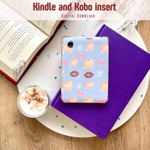 Op de afbeelding: Een lichtblauwe Kindle- en Kobo-hoes met een patroon van harten en lippen. De hoes ligt op een paars boek en een witte schaal. Een open boek met een rode rug en een klein bakje yoghurt staan ook op de schaal. De tekst "Kindle and Kobo insert" staat bovenaan.