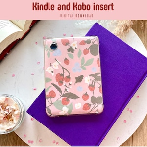 Op de afbeelding: Een roze Kindle- of Kobo-hoesje met een aardbeien- en bloemenpatroon, liggend op een paars boek. De afbeelding bevat ook een open boek en een kleine kaars. De tekst "Kindle and Kobo insert" staat bovenaan.