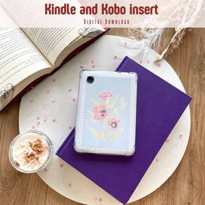Op de afbeelding: Een lichtblauwe Kindle- of Kobo-hoes met een bloemenontwerp, rustend op een paars boek. Een open boek en een kaars zijn ook zichtbaar. De tekst "Kindle and Kobo insert" staat bovenaan de afbeelding.