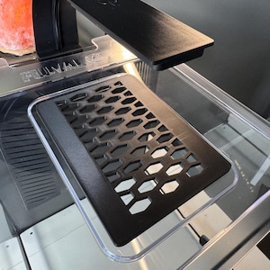 May include: A black aquarium light with a flexible arm is positioned over a clear glass tank. A black, honeycomb-patterned insert sits inside the tank. A pink salt lamp is visible in the background.
