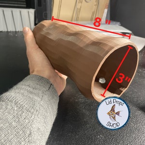 May include: A brown, 3D printed, curved tube with a diameter of 3 inches and a length of 8 inches. The tube is textured and has a smooth, rounded opening. The tube is held in a hand.