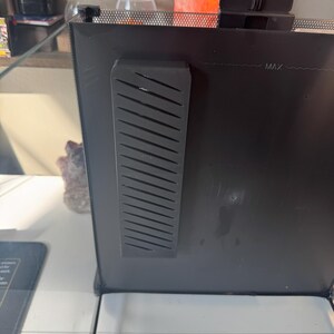 May include: Black terrarium with a rectangular, slotted vent on the side. The top of the terrarium has a mesh screen. The words "MAX" are visible on the side of the terrarium.