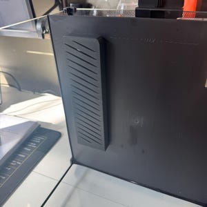 May include: A black computer monitor with a black, rectangular, ridged component attached to the side. The monitor has a maximum level indicator. The monitor is on a white surface.