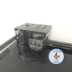 May include: Black aquarium filter with a clear water reservoir and multiple holes on top. The filter is mounted on the edge of a black aquarium. The text "Lid Propz SHOP" is visible on a sticker in the lower right corner of the image.