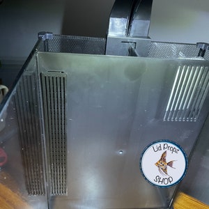 May include: A black aquarium filter with a white sticker that says "Lid Propz Shop" and a picture of a fish. The filter has a black grate on the top and a black grate on the bottom.