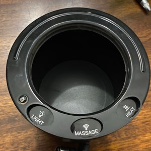 May include: Black round cup warmer with three buttons: Light, Massage, and Heat.