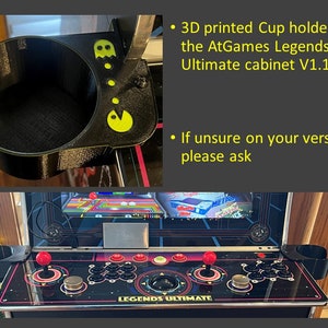 May include: Two black 3D printed cup holders with a Pac-Man design. The cup holders are attached to a black arcade cabinet with a screen displaying a video game. The cabinet has a control panel with buttons and joysticks. The text "LEGENDS ULTIMATE" is printed on the control panel.