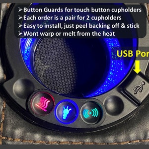 May include: Close-up of a car's center console with a black leather surface. The console features a cupholder with a blue light ring, a USB port, and buttons for heated seats, a light, and a sound system.