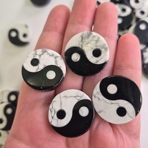 May include: A collection of round Yin and Yang stones. Each stone features a black and white design, with a marble-like texture on the white portion. The stones are held in a hand, with others scattered in the background.