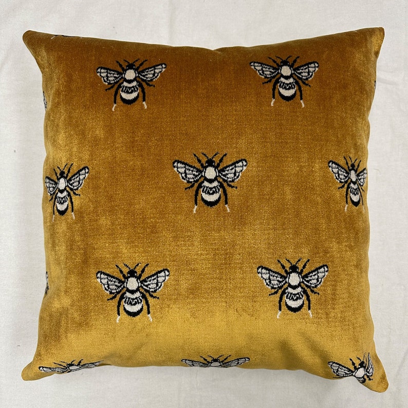 May include: A mustard yellow velvet throw pillow with a repeating pattern of black and white bees.