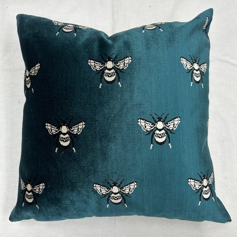 May include: Teal velvet pillow with a repeating pattern of white stylized bumblebees.