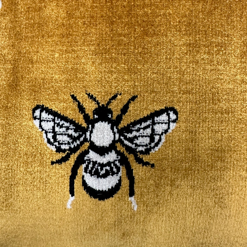 May include: A black and white embroidered bee design on a gold velvet fabric.