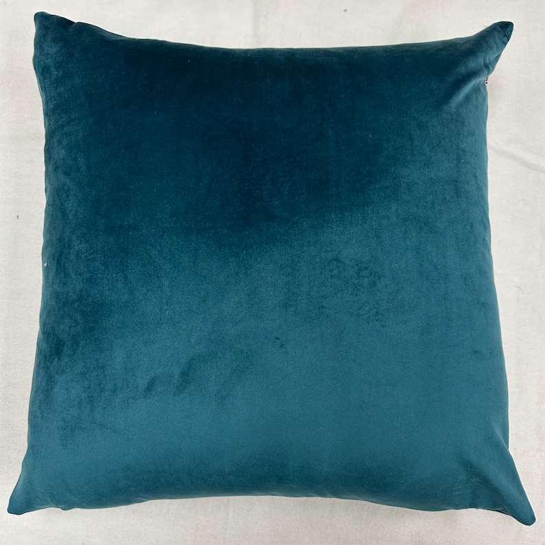 May include: A teal blue velvet pillow with a soft, plush texture. The pillow is square shaped and has a subtle sheen.