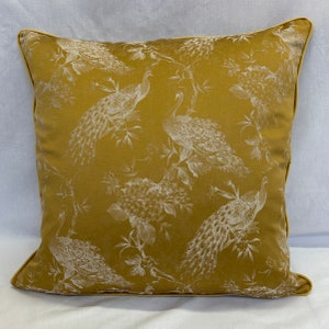 Peut inclure: Un coussin jaune moutarde avec un motif de paon blanc. Le coussin a un léger brillant et une bordure décorative.