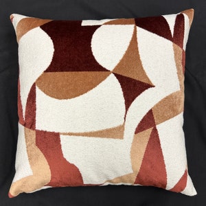 May include: A white throw pillow with a geometric pattern in shades of brown, tan, and red.