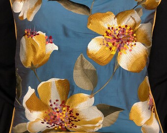 May include: A blue pillow with a yellow, white, and red floral embroidery design. The pillow has a yellow border.