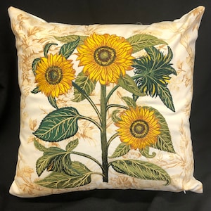 Peut inclure: Un oreiller blanc avec un motif floral représentant un groupe de tournesols avec des feuilles et des tiges vertes. Les tournesols sont jaunes avec des centres bruns.