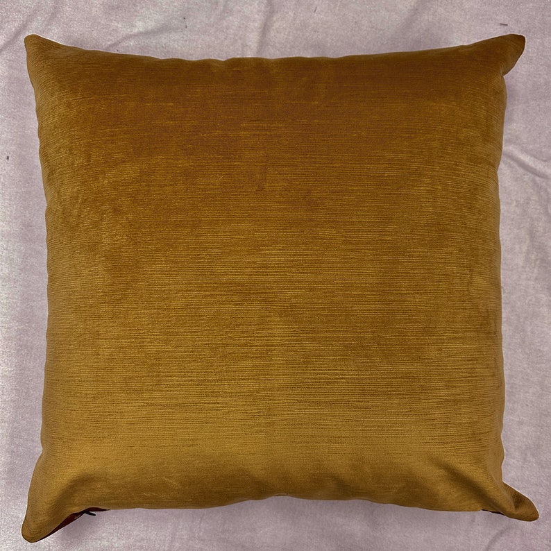 May include: A solid mustard yellow throw pillow with a soft, velvety texture. The pillow is square shaped and has a subtle sheen.