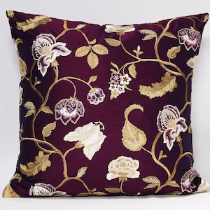 May include: A purple cushion with a floral pattern embroidered in gold and white. The flowers are stylised and have a vintage look.